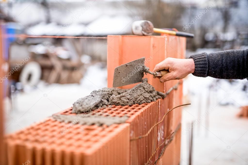 Construction site on a winter day with worker building brick walls with mortar and bricks