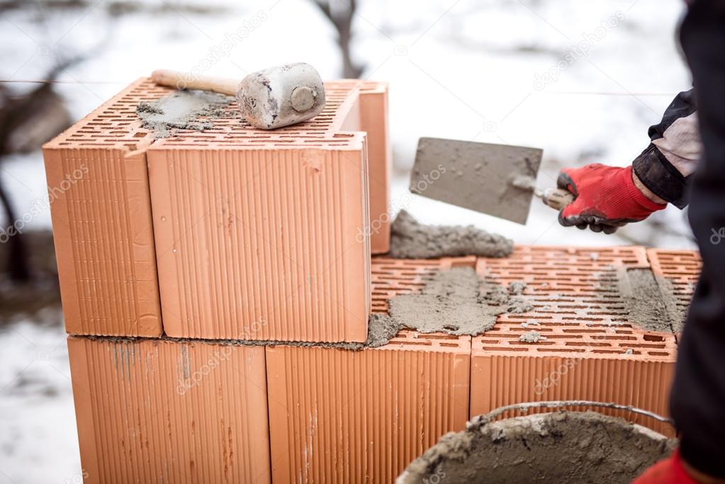 Construction site of new house during winter, man working with bricks and cement, building walls