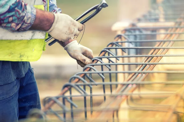 Mãos do trabalhador usando fio de aço e alicates para fixar barras no local de construção e se preparando para derramamento de concreto — Fotografia de Stock