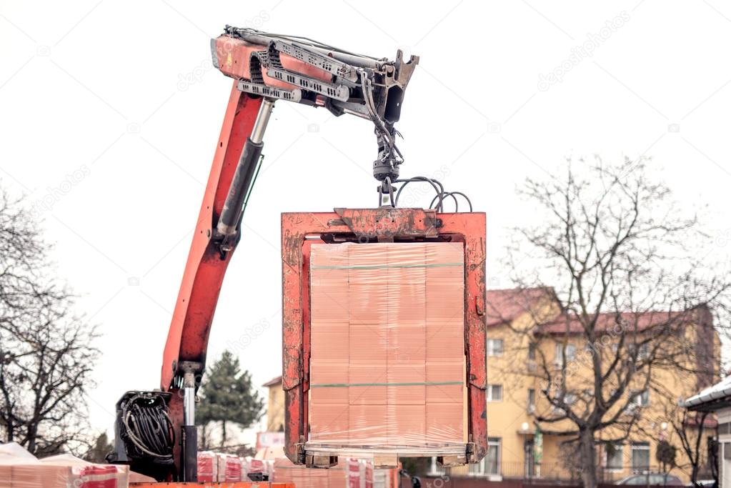 Crane or industrial forklift delivers a brick pallet at building construction site, isolated on white sky 