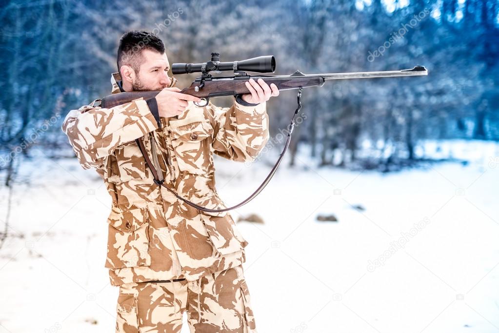 Military man holding a sniper rifle and aiming at enemy on the battlefield