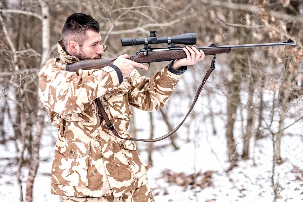 Hunter with sniper aiming and shooting in the forest during winter hunting season