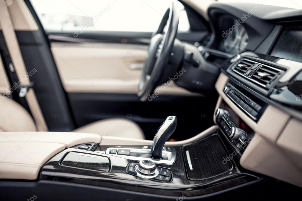 Modern beige and black interior of modern car, close-up details of automatic transmission and gear stick against steering wheel background and dashboard