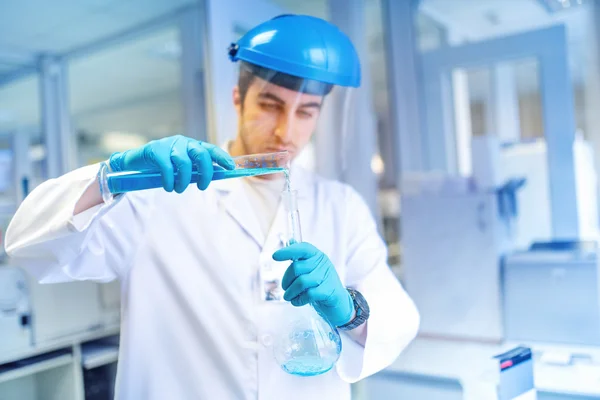 Joven científico masculino aprendiendo y haciendo experimentos en laboratorio químico con sustancias líquidas — Foto de Stock