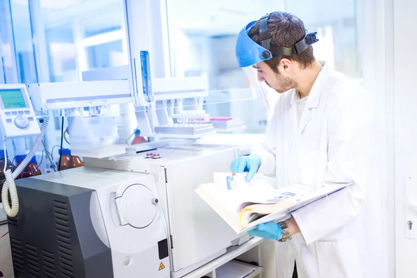 Cientista que usa o manual para programar uma maquinaria química do computador no laboratório — Fotografia de Stock