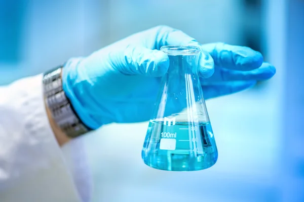 举行与蓝色液体的玻璃，做这样的实验和开展探针在特殊实验室的科学家手 — 图库照片