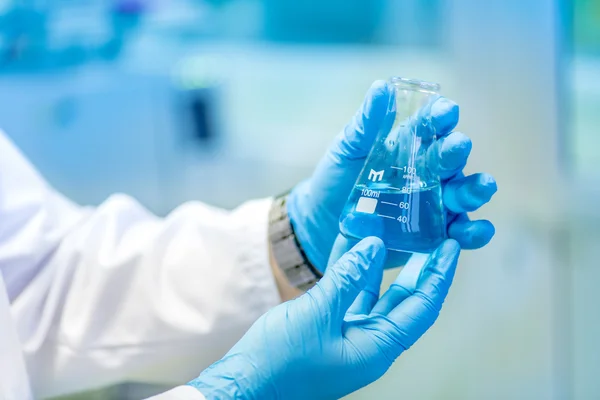 Médico sosteniendo un tubo de ensayo, un frasco con líquido azul en un laboratorio especial preparándose para experimentos y tratamientos — Foto de Stock