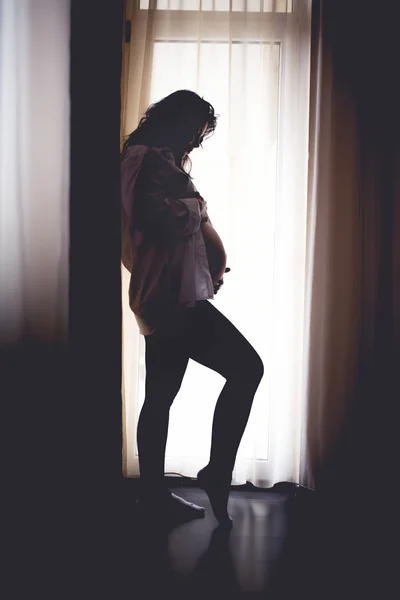 Silhouette of beautiful pregnant woman holding hands on baby, cozy portrait of beautiful mother — Stok fotoğraf