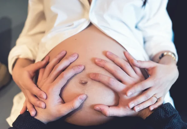 Ouders hand in hand op zwangere buik, liefdevolle de baby. Moederschap Concept. Zachte effect op foto. — Stockfoto