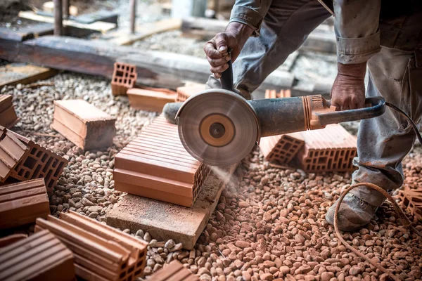 Engenheiro industrial trabalhando no corte de tijolos no local de construção, usando um moedor, serra de mitra elétrica com lâmina circular afiada — Fotografia de Stock