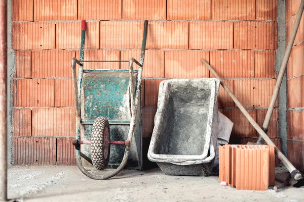 Camadas de tijolo com argamassa, carrinho de mão e misturador de cimento no canteiro de obras — Fotografia de Stock