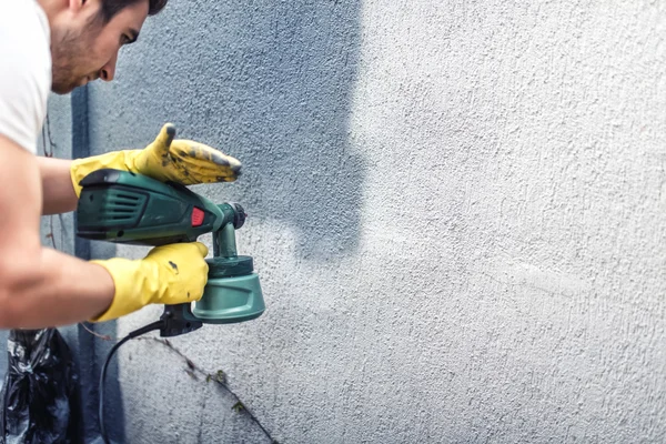 Человек красит серую стену, ремонтирует наружные стены нового дома — стоковое фото