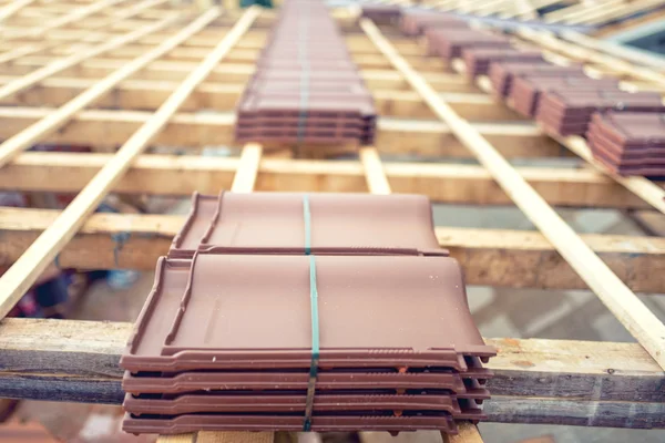 Roof under construction with stacks of brown roof tiles prepared on wooden structure — Stock Photo, Image