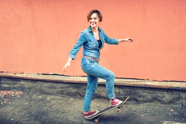 Арцетический портрет брюнетки симпатичной девушки на скейтборде, смеющейся и хорошо проводящей время. Здоровая концепция современной жизни, девушка-хипстер со скейтбордом на крыше — стоковое фото