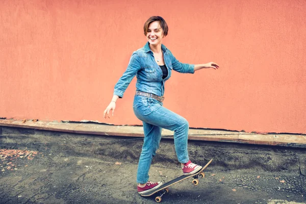 Artsy portrait of a brunette cute girl on a skateboard, laughing and having a good time. Healthy concept of modern life, hipster girl with skateboard on rooftop — Stok fotoğraf