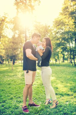 Happy familiy in park, mother and father holding and kissing a few months old son, kid. Infant portrait and happy family concept in park