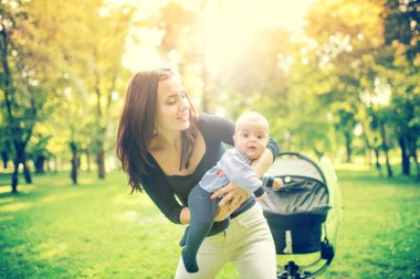 Happy mother holding and playing with newborn son in park. Happy woman holding infant, little kid and child