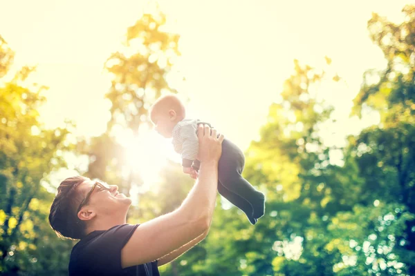 Lycklig far håller liten unge i armar, kasta barnet i luften. begreppet lycklig familj, vintage effekt mot ljus — Stockfoto