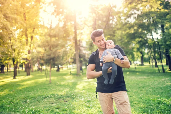 Szczęśliwy ojciec trzyma małego syna, niemowlę chłopiec w słoneczny dzień w parku. — Zdjęcie stockowe