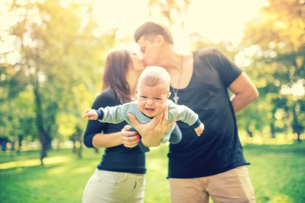 Cuplu tânăr căsătorit care ține copilul nou-născut și se sărută. Familie fericită, conceptul de zi al tatălui și al mamei . — Fotografie, imagine de stoc