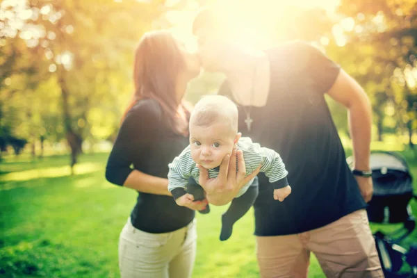 Happy father holds newborn baby on arm while kissing the mother of child. happy family in park, newborn kid and happiness — Stock fotografie