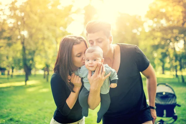 Mommy and daddy holding baby, 3 months old newborn and kissing him. Happy family with father, mother and infant. Vintage effect on photo — Zdjęcie stockowe