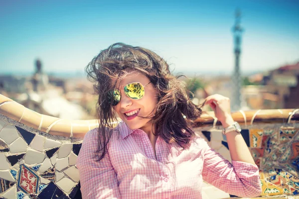 Portrait of smiling, gorgeous brunette girl with sunglasses on a windy day. Beautiful woman smiling and playing with hair on rooftop of building — Stock Photo, Image