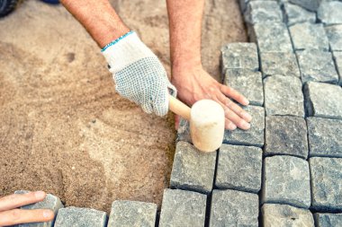 Construction worker installing stone blocks, creating pavement on road, sidewalk or path. clipart