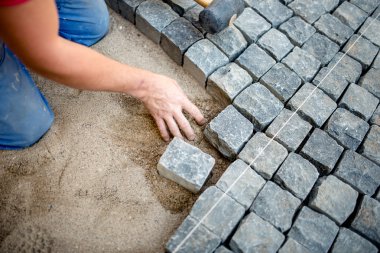 industrial construction worker laying cobblestones and stone blocks on pavement