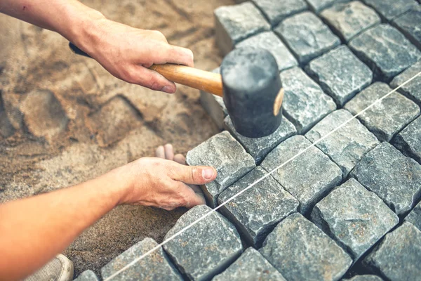 Detailní záběr stavebního dělníka instalujícího a pokládajícího dlažební kameny na terasu, silnici nebo chodník. Dělník pomocí kamenů a gumového kladiva stavět kamenný chodník — Stock fotografie