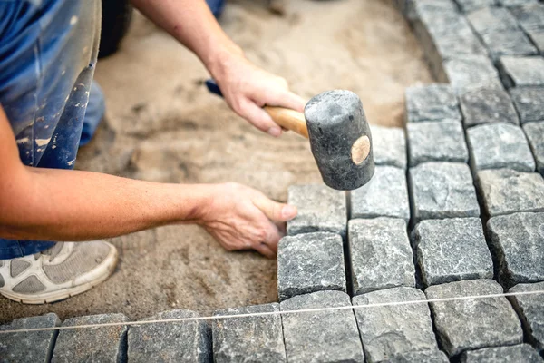 Worker creating pavement using cobblestone blocks and granite stones — Stock Fotó