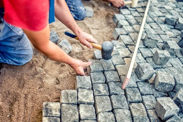 Paving pavement with granite stones, workers using industrial cobblestones for paving terrace, road or sidewalk — Zdjęcie stockowe