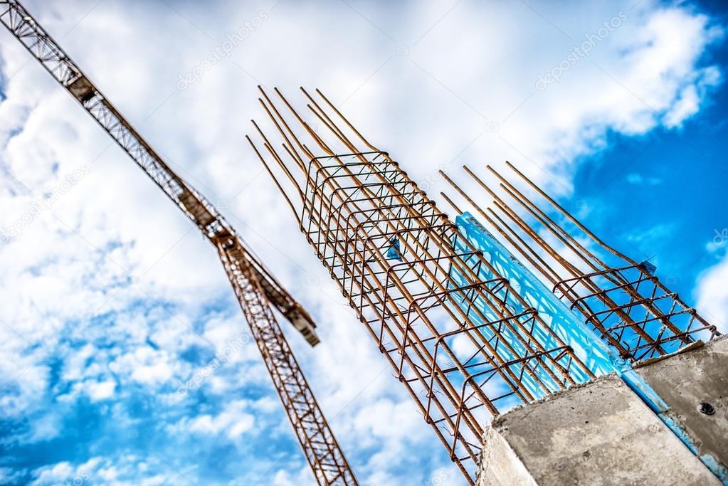Concrete pillars on industrial construction site. Building of skyscraper with crane, tools and reinforced steel bars