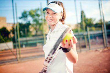 Tenis oynarken, raket ve top tutan bir kadın portresi. Tenis kortunda beyaz t-shirt ve şapka giyen çekici esmer kız