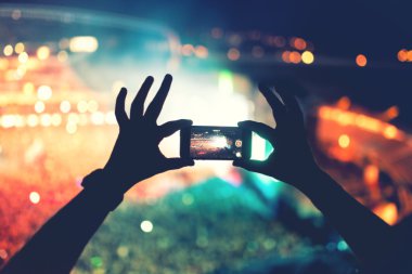 Pop konser, festival fotoğraf ve video çekmek için kamera telefon kullanarak eller silüeti. Fotoğraf üzerinde yumuşak etkisi