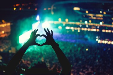 Heart shaped hands at concert, loving the artist and the festival. Music concert with lights and silhouette of a man enjoying the concert