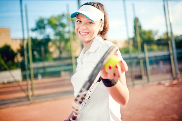 Tenis oynarken, raket ve top tutan bir kadın portresi. Tenis kortunda beyaz t-shirt ve şapka giyen çekici esmer kız — Stok fotoğraf
