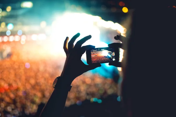 Silhueta de um homem usando smartphone para fazer um vídeo em um concerto. Estilo de vida moderno com hipster tirando fotos e vídeos no concerto local. Foco principal na câmera e luzes . — Fotografia de Stock