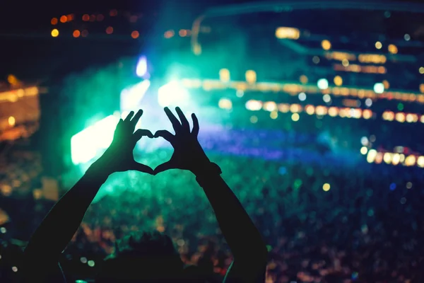 Mani a forma di cuore in concerto, amando l'artista e il festival. Concerto musicale con luci e silhouette di un uomo che si gode il concerto — Foto Stock