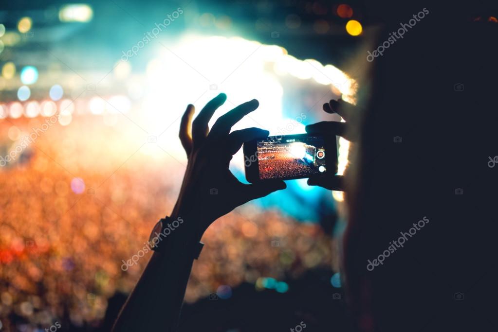 Silhouette of a man using smartphone to take a video at a concert. Modern lifestyle with hipster taking pictures and videos at local concert. Main focus on camera and lights.