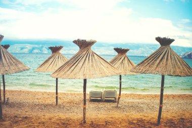 Instragram retro effect on photo, beach umrellas with straws and shade on beach, coastline landscape with seaside or ocean background clipart