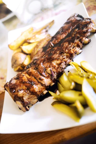 Vepřová žebírka s barbecue omáčkou, zlaté brambory a okurky. Hlavní jídlo v restauraci, hovězí nebo vepřová pochoutka — Stock fotografie