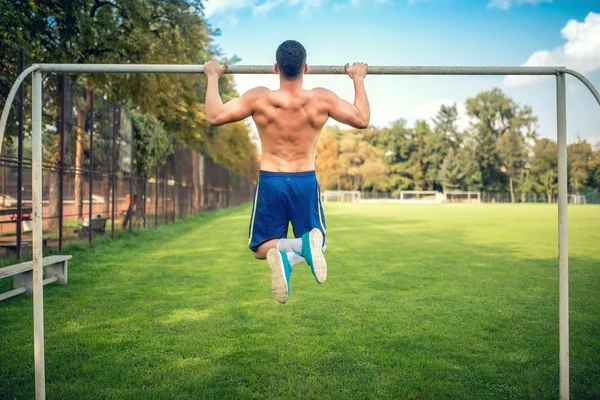 Sexy culturista haciendo ejercicio en el parque, haciendo flexiones de mentón y flexiones. Entrenamiento de fitness masculino al aire libre —  Fotos de Stock