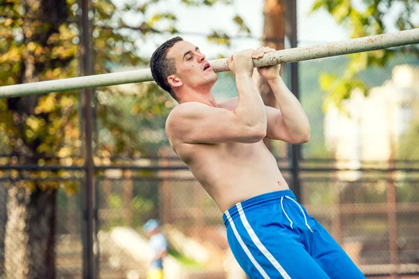 Cross fit training concept with muscular fitness player and personal trainer working out in park. Athletic man doing pull ups — Stock Photo, Image