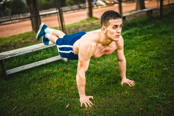 Homme athlétique pendant l'entraînement dans le parc. Fitness entraîneur personnel faisant des pompes sur l'herbe. Concept d'entraînement cross-fit — Photo