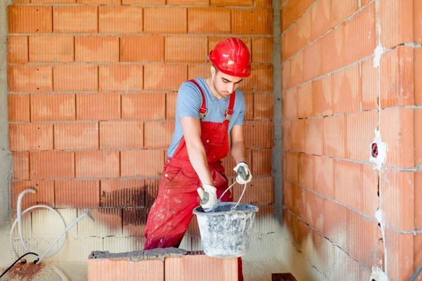 Fiatal munkavállaló, épület építőmunkás falak és házak. Webhelyen dolgozik kerek-perec — Stock Fotó