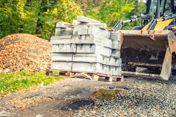 Escavadeira ou bulldozer transportando paletes com pedras de pavimentação ou bordas da calçada — Fotografia de Stock