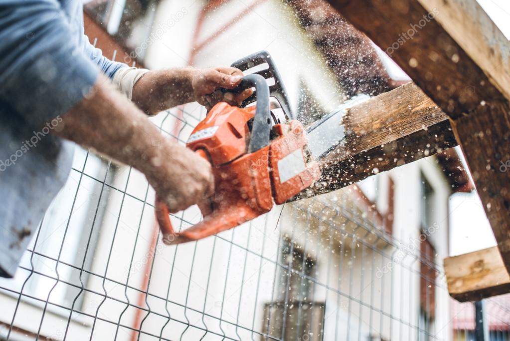 worker using an industrial chainsaw for cutting timber wood at construction site