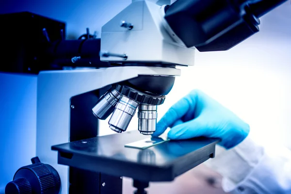 Muestras de análisis de químicos con microscopio y guantes de goma. Químico médico en el campo farmacéutico examinando — Foto de Stock