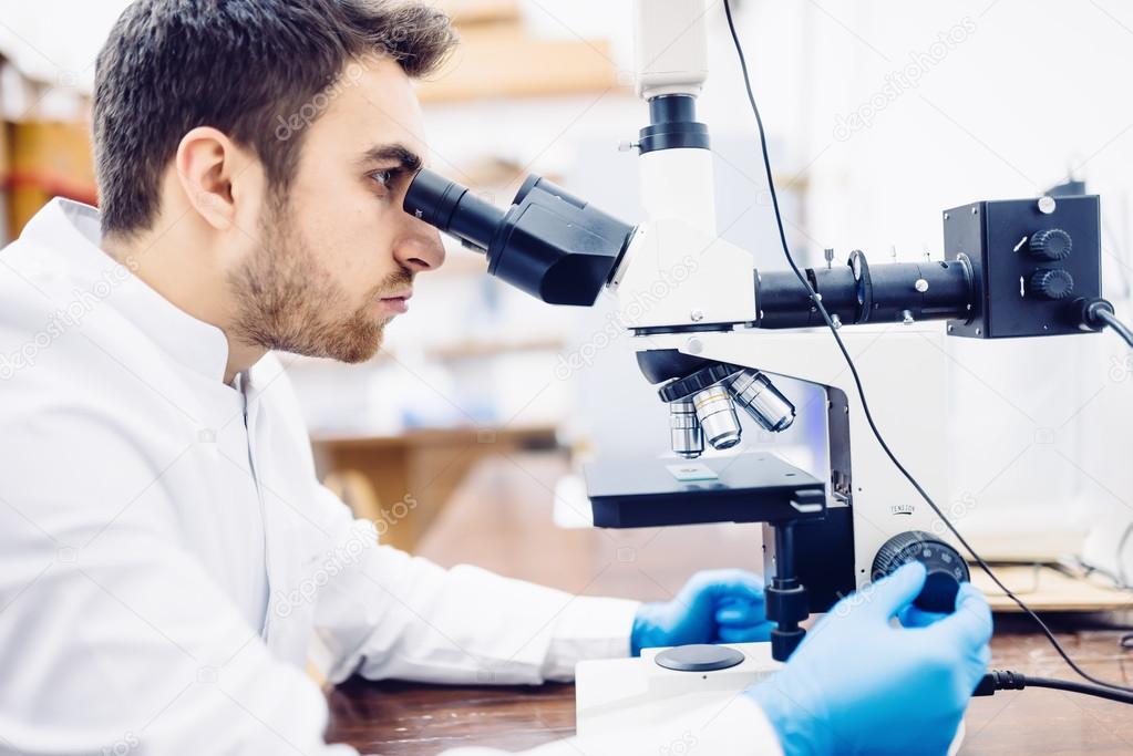 Male scientist, chemist working with microscope in pharmaceutical laboratory, examinating samples